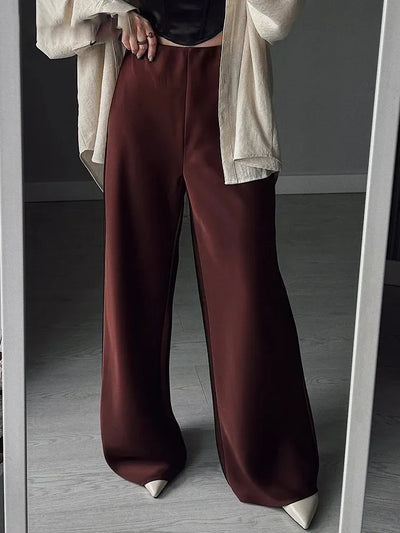 Maroon high-waisted wide-leg satin pants styled with beige coat and white pointed-toe heels