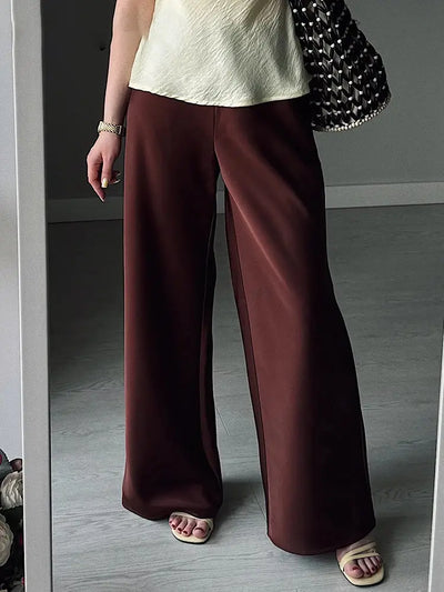 Deep maroon wide-leg satin pants worn with cream top white sandals and woven bag