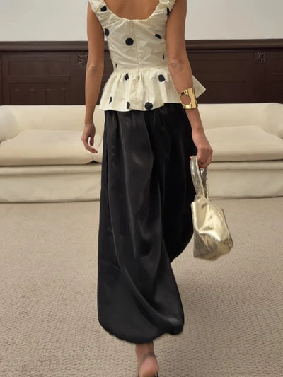 Back view of woman wearing black wide-leg satin pants with white polka-dot peplum top and gold clutch