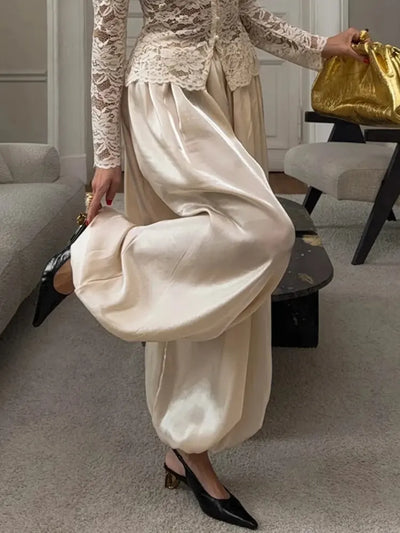 Woman standing in ivory wide-leg satin pants paired with a white lace long-sleeve top and black slingback heels
