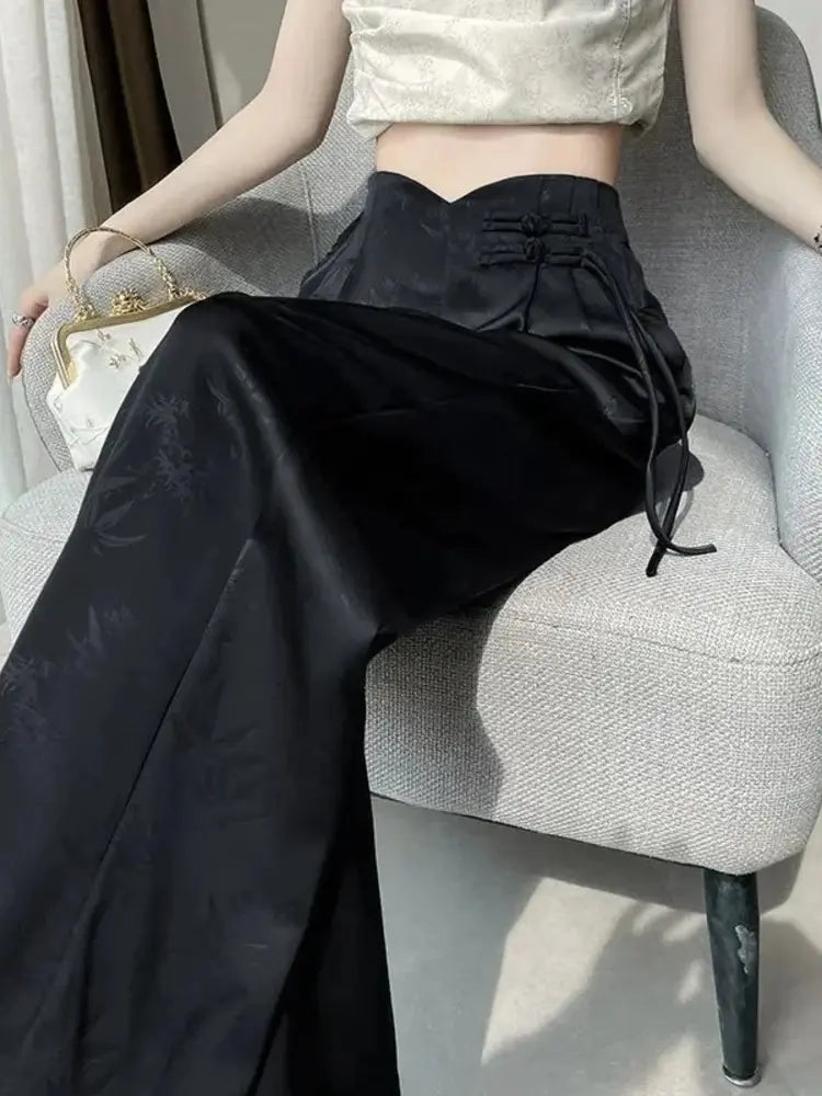 Black high-waist wide-leg satin pants with frog closures and sweetheart waistband, worn seated