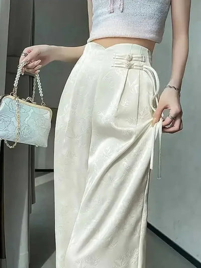 Cream high-waist wide-leg satin pants with frog-button closures and ribbon ties, front view standing