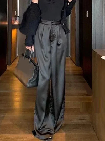 Full-length front view of black pleated wide-leg satin pants worn with black cardigan