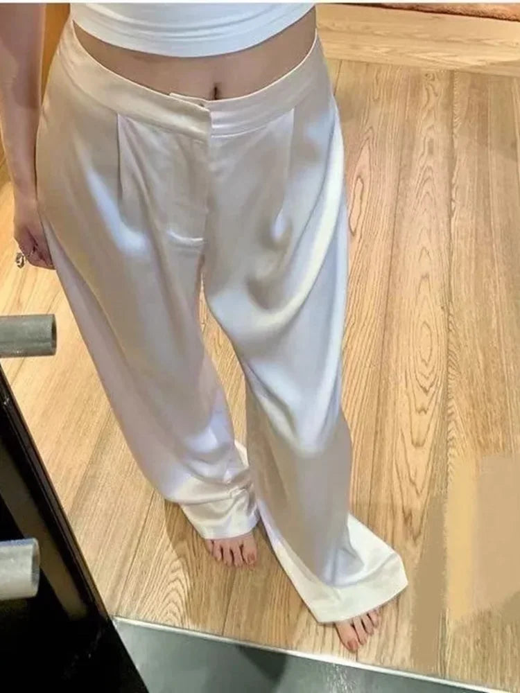 Ivory low-rise pleated satin wide-leg pants worn barefoot on wood floor, front view