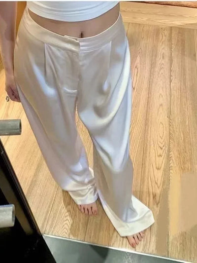 Ivory low-rise pleated satin wide-leg pants worn barefoot on wood floor, front view