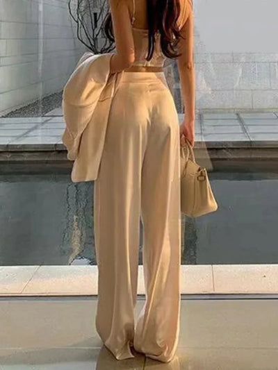 Ivory pleated wide-leg satin pants styled with a cropped cami and blazer, rear view outdoors