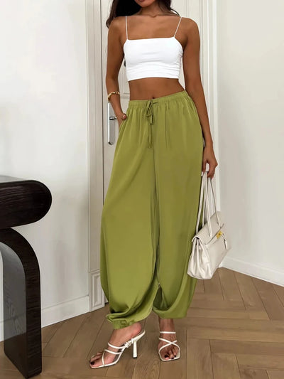 Woman standing in olive green balloon satin pants paired with white crop top and heeled sandals