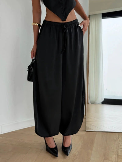 Woman standing in black satin wide-leg jogger pants paired with cropped black top and pumps