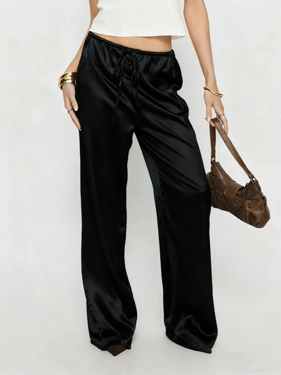 Front view of black low-rise wide-leg satin pants with drawstring waist and high-shine finish