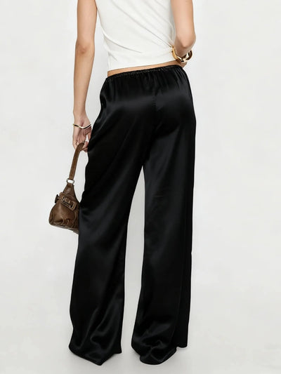 Back view of black low-rise wide-leg satin pants showing elastic waistband and fluid drape