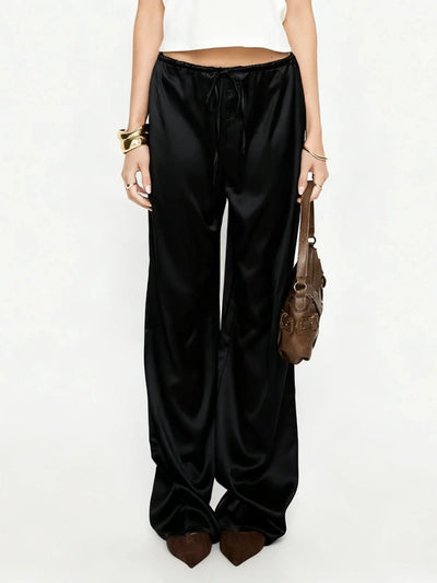 Full-length front view of black wide-leg satin pants styled with white crop top and brown pointed flats