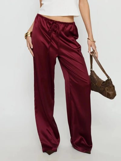 Woman wearing burgundy wide-leg satin pants with drawstring waist paired with white crop top and brown bag
