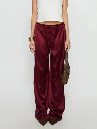 Close-up of burgundy satin wide-leg pants with elasticated drawstring waistband and flowing full-length silhouette
