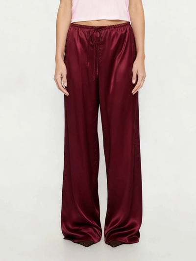Front view of deep burgundy wide-leg satin pants with drawstring tie worn with pink crop top