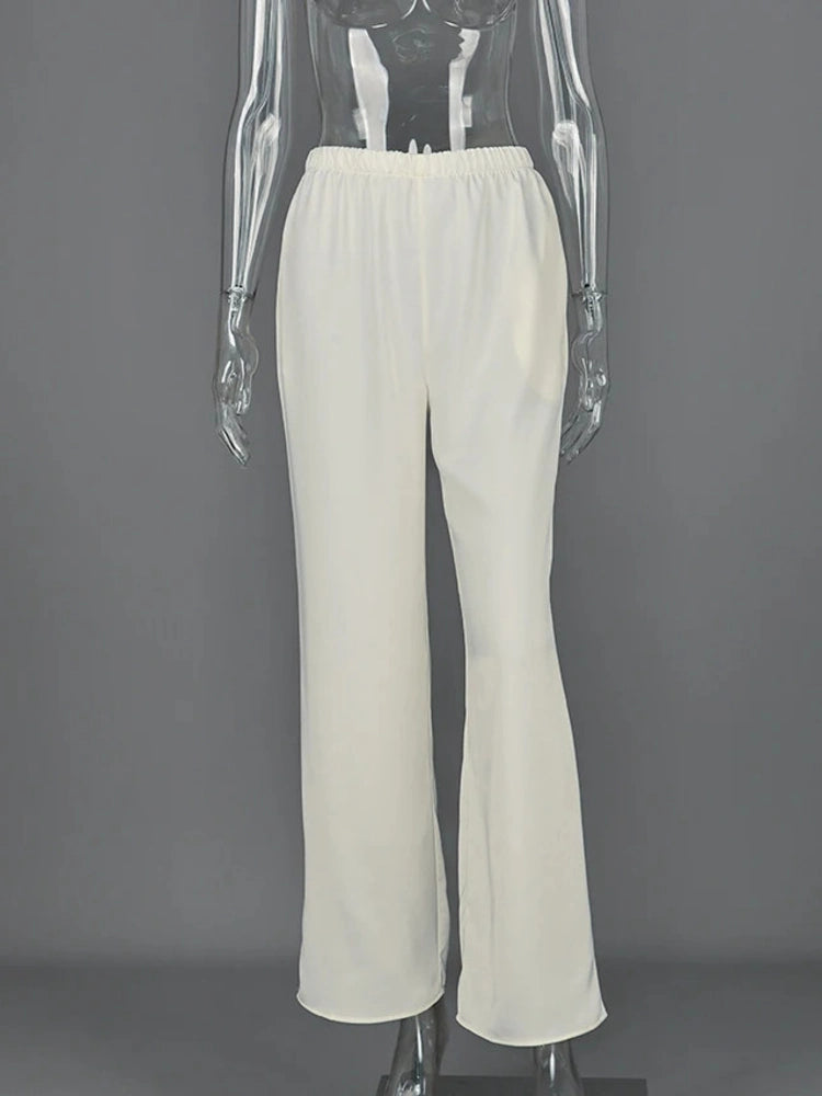 Woman holding a gray Hermes Birkin bag wearing off-white straight-leg satin pants and white tee