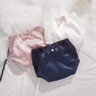 Pink, white, and navy satin lace panties with ribbon bows, grouped flat lay