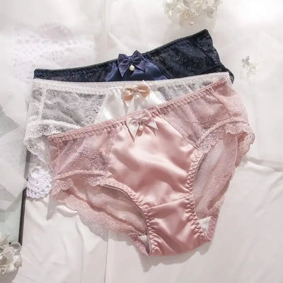 Three satin lace panties in navy, white, and pink stacked on white bedding