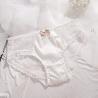 White satin panties with sheer lace overlay and champagne ribbon bow, flat lay
