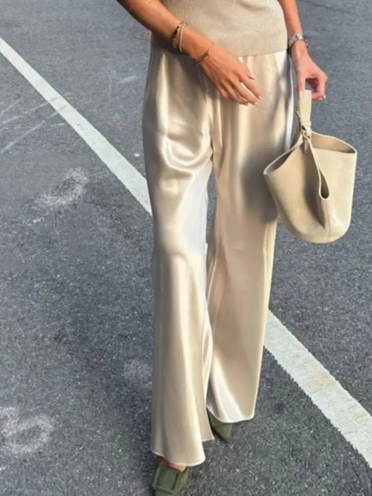 Woman walking in champagne satin straight-leg pants with mules and a bucket bag