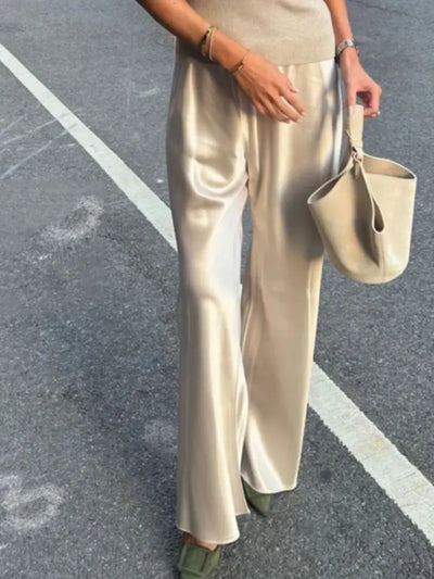 Woman walking in champagne satin straight-leg pants with mules and a bucket bag