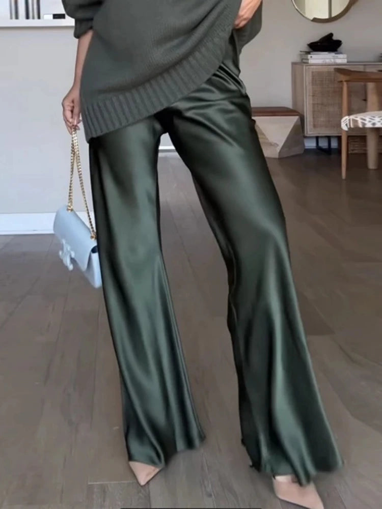 Olive green flared satin wide-leg pants styled with an oversized gray knit top and nude heels, full-length view