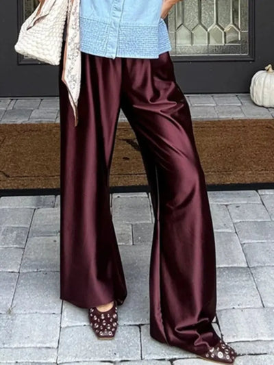 Woman wearing oxblood wide-leg satin pants with blue top and studded mules outdoors