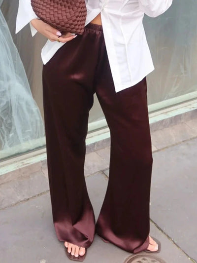 Close-up of oxblood glossy wide-leg pants styled with white shirt and open-toe slides