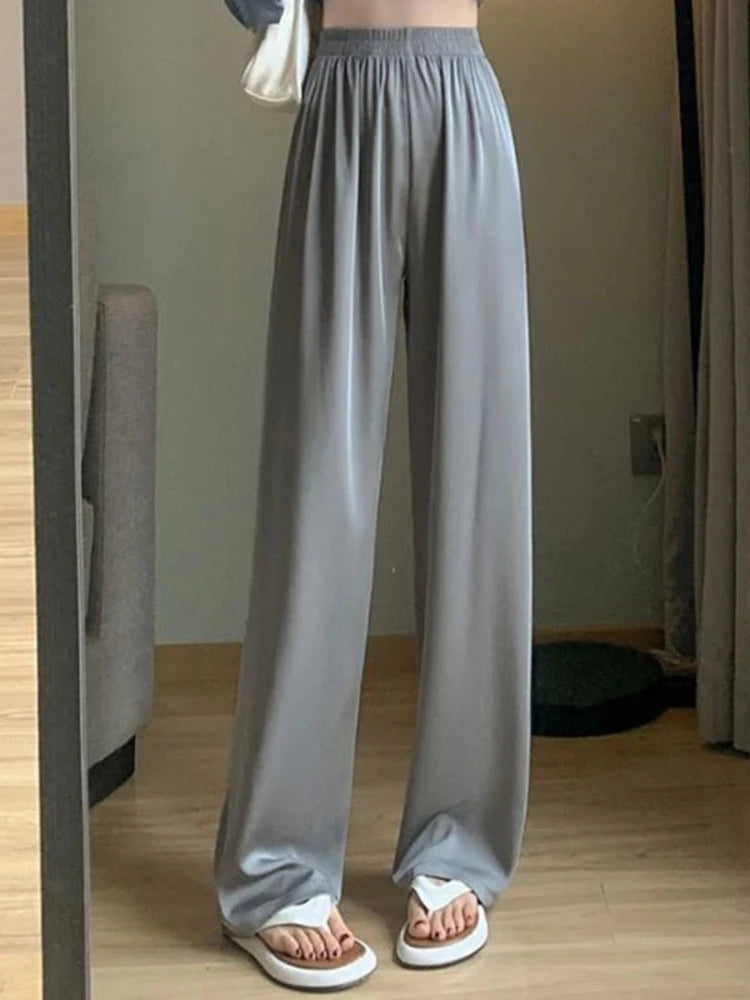 Gray wide-leg satin pants with smocked high waist worn with flat sandals, floor-length drape