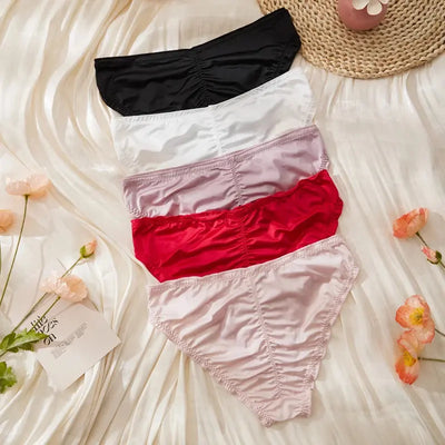 Five satin ruched panties stacked showing back panels in black, white, lavender, red, and light pink on cream fabric