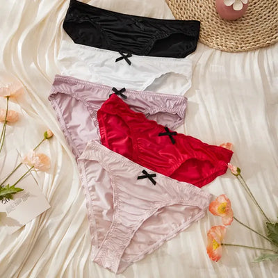 Front view of five ruched satin panties fanned out showing bow details in black, white, lavender, red, and light pink