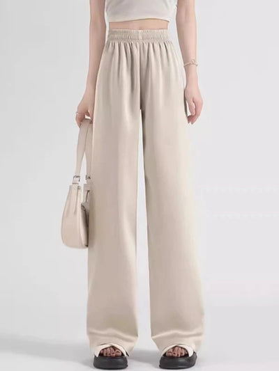 Woman wearing beige high-rise smocked waistband wide-leg satin pants with white crop top and sandals
