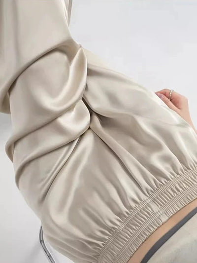 Close-up of smocked elasticized waistband on beige wide-leg satin pants showing fabric drape