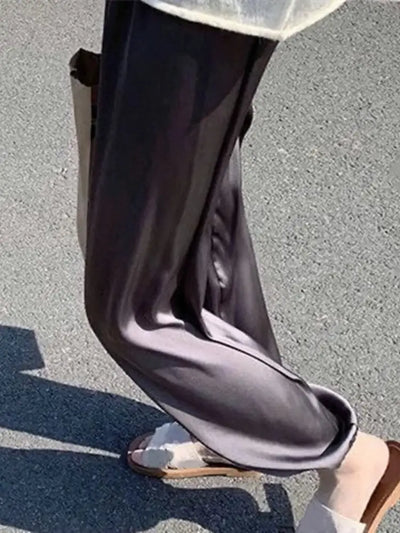 Close-up of gray wide-leg satin pants with cuffed hem worn with flat sandals outdoors