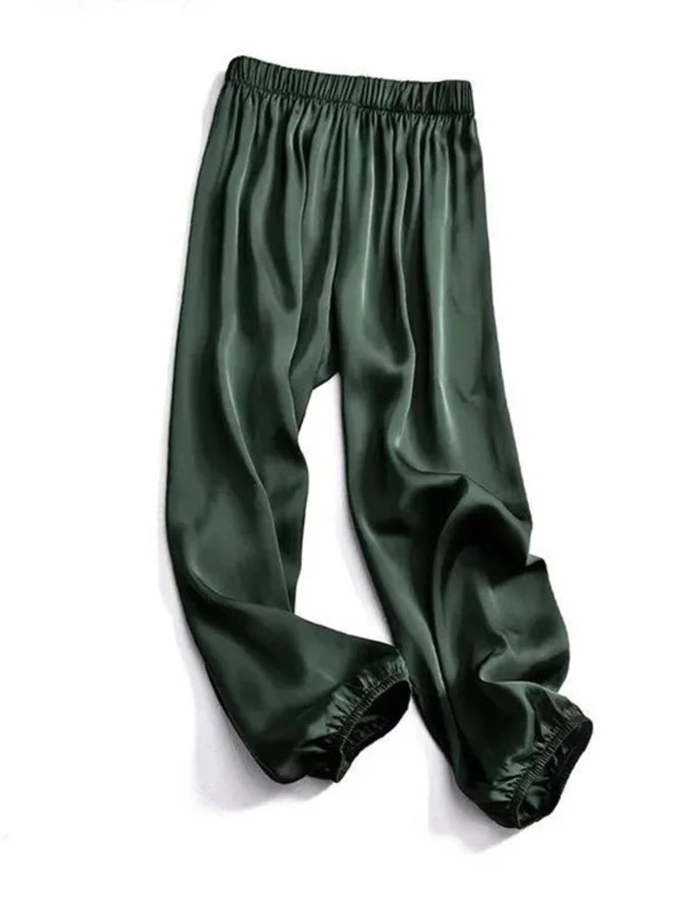 Forest green satin pants with elastic waistband and cuffed ankle hem, flat lay on white background