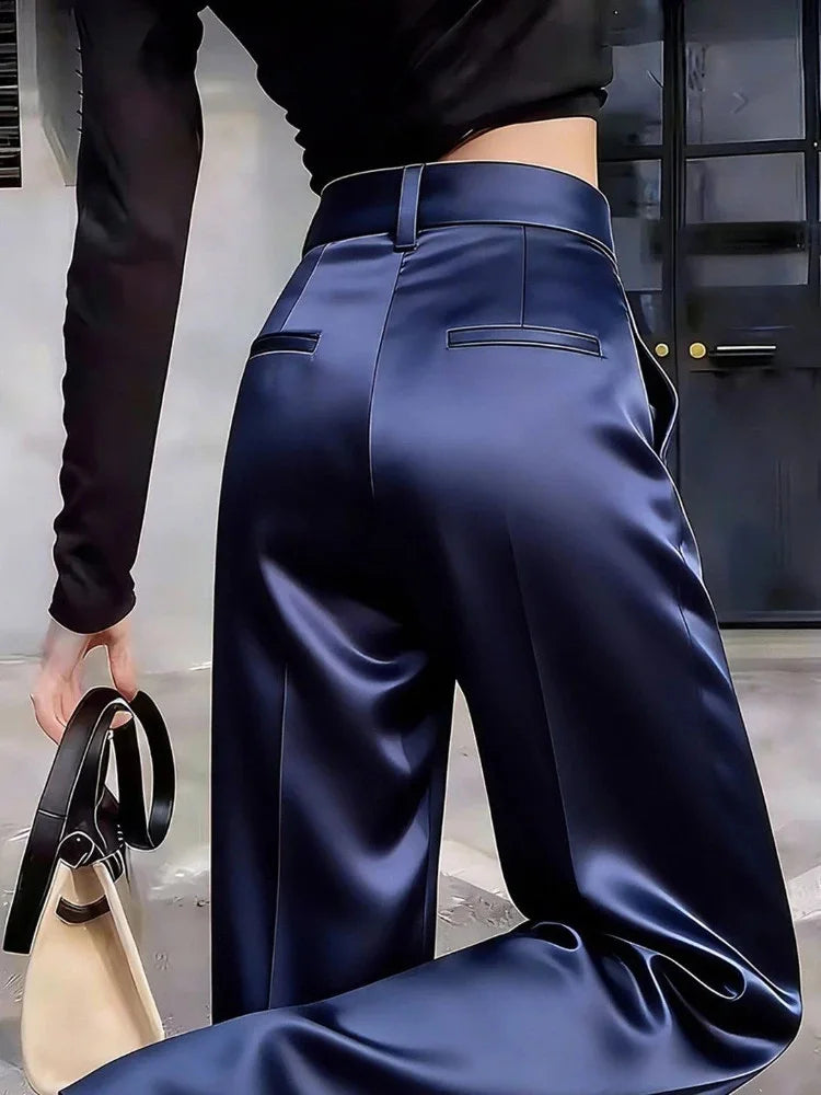 Back view of navy high-rise wide-leg satin pants with welt pockets and belt loops, paired with a black crop top and a structured handbag