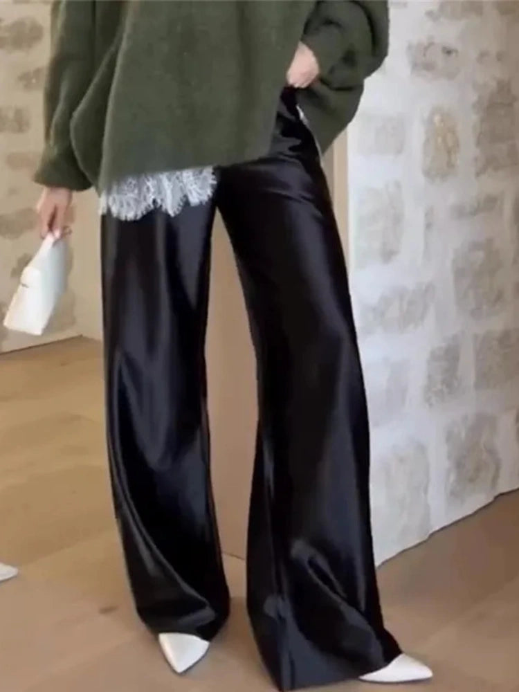 Black wide-leg satin pants with white scalloped lace hem trim, styled with a green oversized knit and white pointed mules