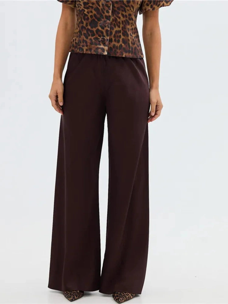 Woman wearing deep brown high-rise wide-leg satin pants with a leopard print top and pointed heels
