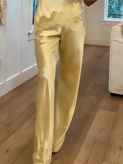 Close-up side view of pale yellow satin wide-leg pants with scalloped lace waistband trim indoors