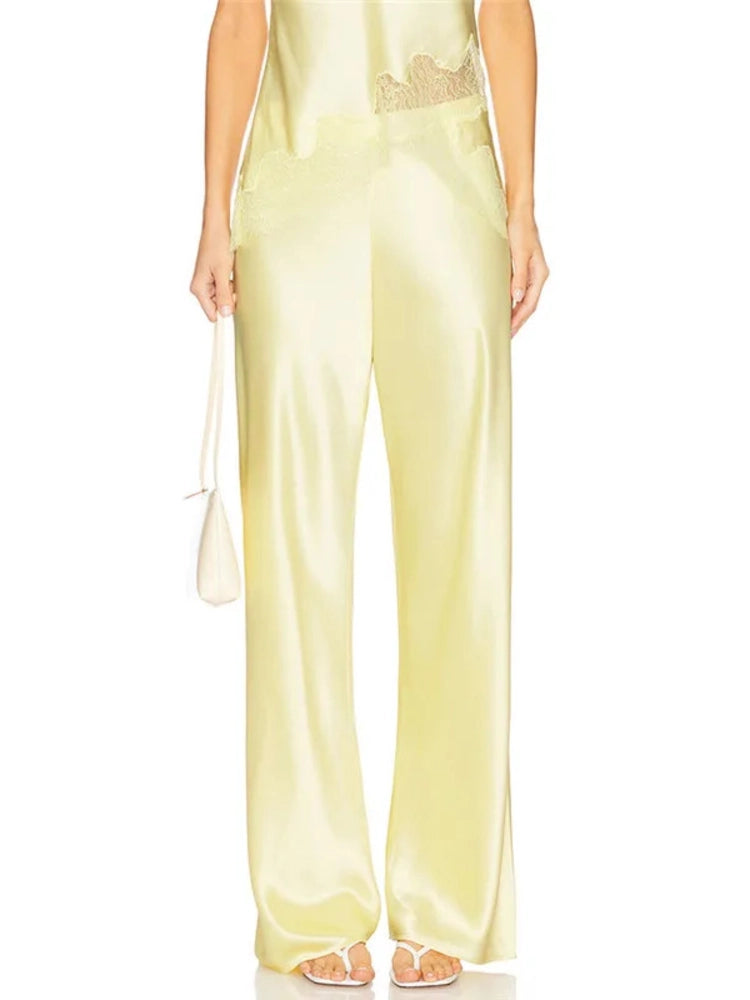 Close-up side view of pale yellow satin wide-leg pants with scalloped lace waistband trim indoors