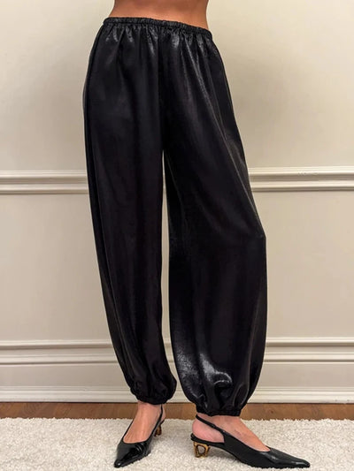 Front view of black glossy balloon-leg pants with elastic waist and ankle cuffs worn with slingback heels