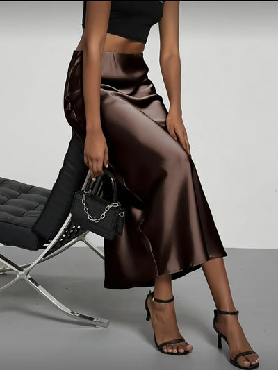 Woman in chocolate brown high-waist satin midi skirt, black crop top, strappy heels, small bag