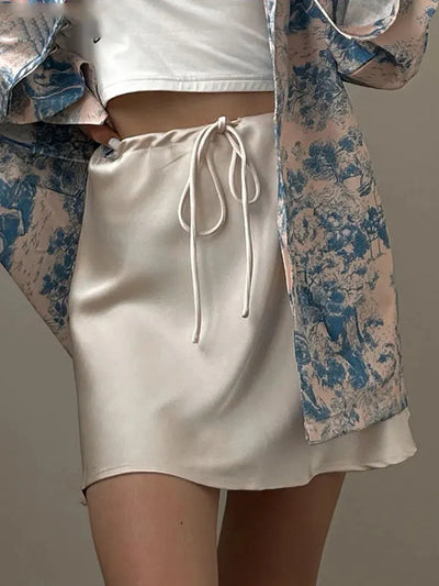 Cream satin mini skirt with front drawstring tie, worn under a blue floral open jacket and white crop top