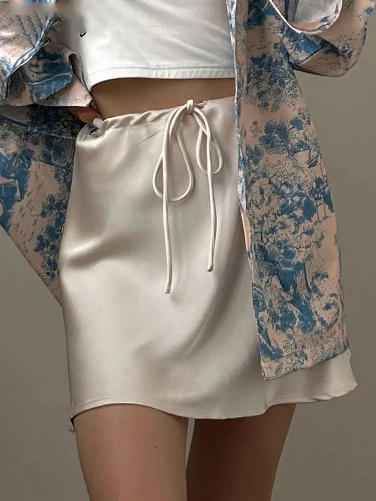 Close-up of cream satin mini skirt with drawstring waist and gathered front detail, styled with black bag