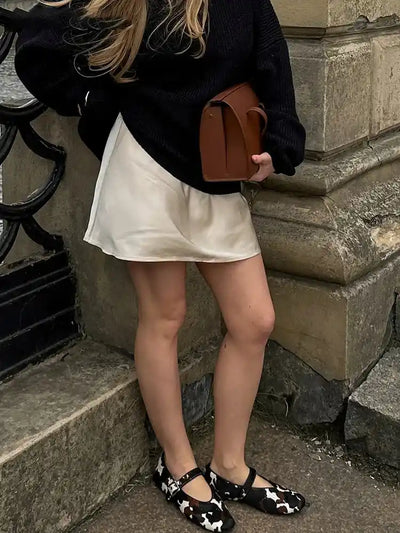 Cream satin mini skirt with drawstring waist worn with black knit sweater, brown bag, and cow-print Mary Janes
