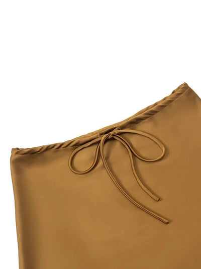 Close-up detail of drawstring bow tie at the waist of a camel-tone satin mini skirt
