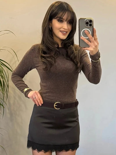 Woman smiling in brown long-sleeve top and black lace-hem mini skirt with gold buckle belt