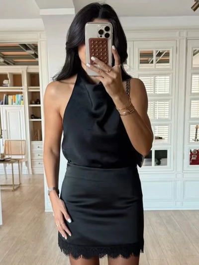 Mirror selfie showing black halter top with a black lace-hem satin mini skirt, hand on hip