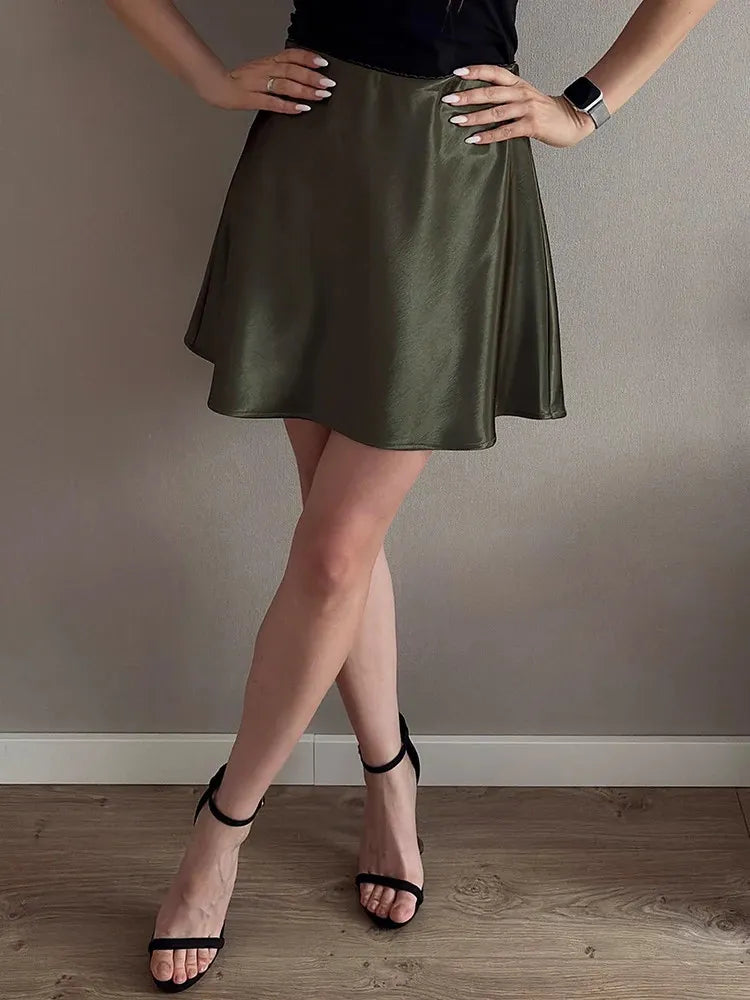 Woman wearing an olive green A-line mini satin skirt with black strappy heels