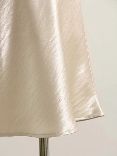 Close-up of ivory satin mini skirt hem showing glossy fabric drape and finish