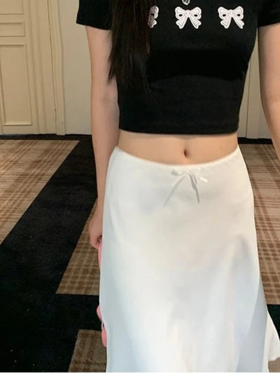 White satin midi skirt with bow detail at waist, paired with black bow-print crop top